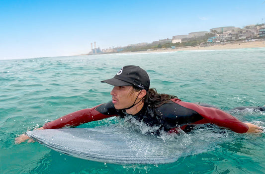 Surfer wearing surf hat with chin strap on while paddling 6