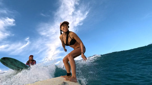 Smiling surfer girl wearing the Ride On Surf Hat while riding a wave while surfer friend also wearing a Ride On Surf Baseball Cap smiles and watches from the line up. 3